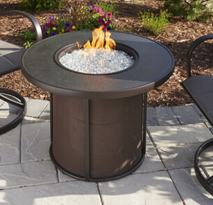 Round gas fire pit on stone patio with two patio chairs