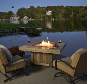 Square gas fire pit placed on dock with two deck chairs and two glasses of wine