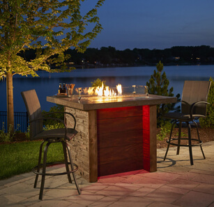 Bar-height gas fire pit table on patio at night with two outdoor bar chairs