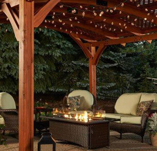 Flames over fire pit table, surrounded by cushioned wicker seating on covered patio Flames over fire pit table, surrounded by cushioned wicker seating on covered patio
