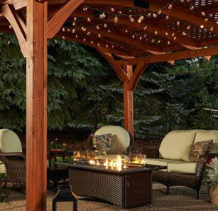 Flames over fire pit table, surrounded by cushioned wicker seating on covered patio