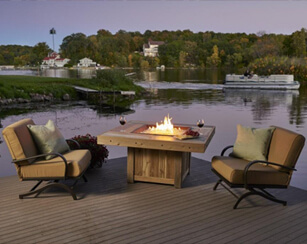 Two cushioned, aluminum chairs, outdoor fire table on patio with pond in background