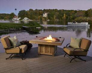 Two cushioned, aluminum chairs, outdoor fire table on patio with pond in background Two cushioned, aluminum chairs, outdoor fire table on patio with pond in background