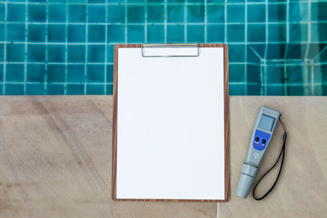 blank white paper on clipboard on the side of inground pool next to a digital water tester