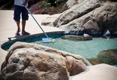 man dipping a skimmer into an in-ground pool