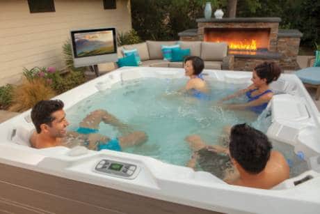 Four people in hot tub with outdoor TV screen in background