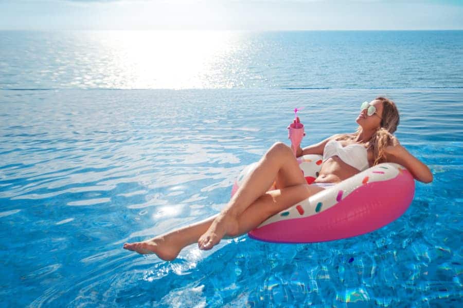 female in bikini at the swimming pool with drink laying on an inflatable pool float