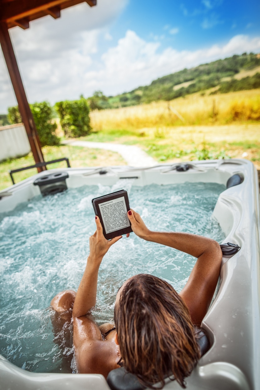 young woman relaxing in a hot tub reading an electronic book