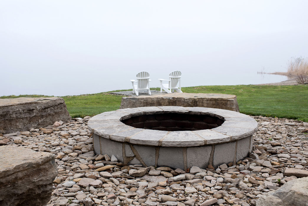 A beautiful stone campfire pit surrounded by gravel and stone benches in a backyard