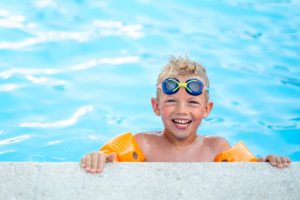 Smiling Child In Swimming Pool Wearing Goggles And Inflatable Armbands