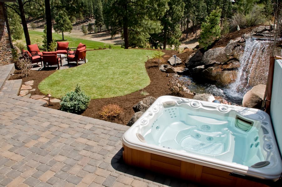Square hot tub in the backyard next to small waterfall